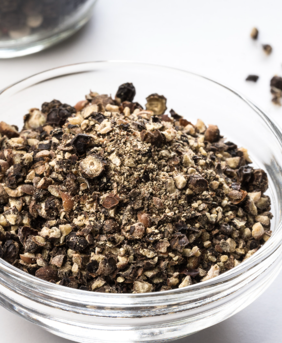 Close-up of a glass bowl filled with a mixture of dark and light ground herbs or spices on a white surface.