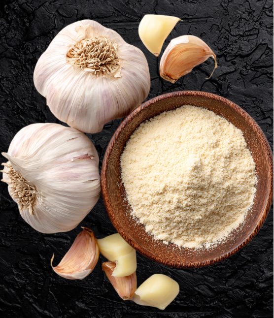Bowl of garlic powder with whole garlic bulbs on a dark surface