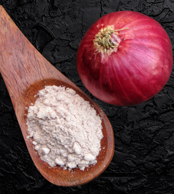 Wooden spoon with onion powder and a red onion on a dark surface
