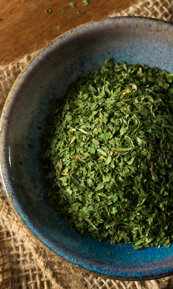 Blue ceramic bowl filled with green dried herbs on a textured surface